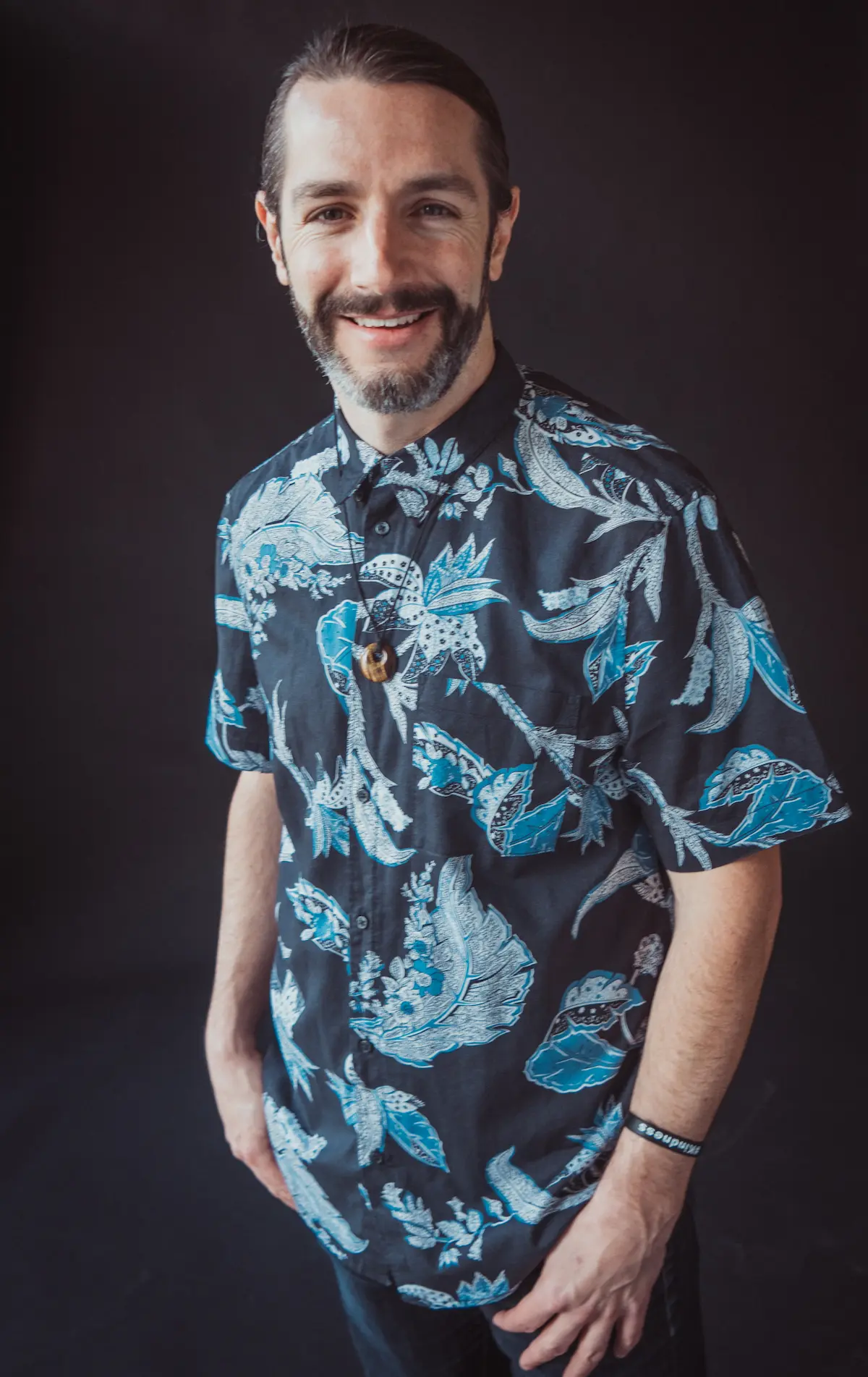 Portrait of Patrick Mallan smiling against a dark backdrop