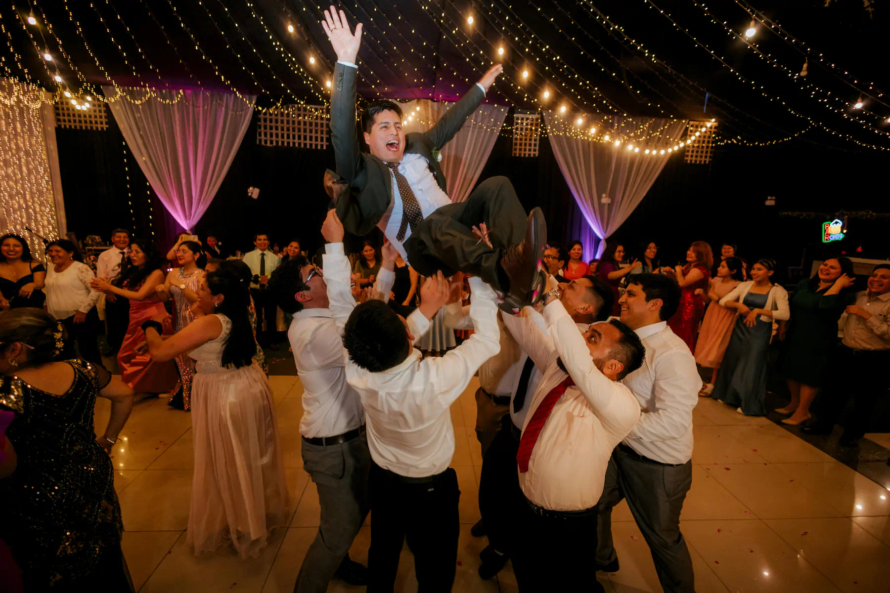 Wedding guests lifting the groom above the dance floor during the reception